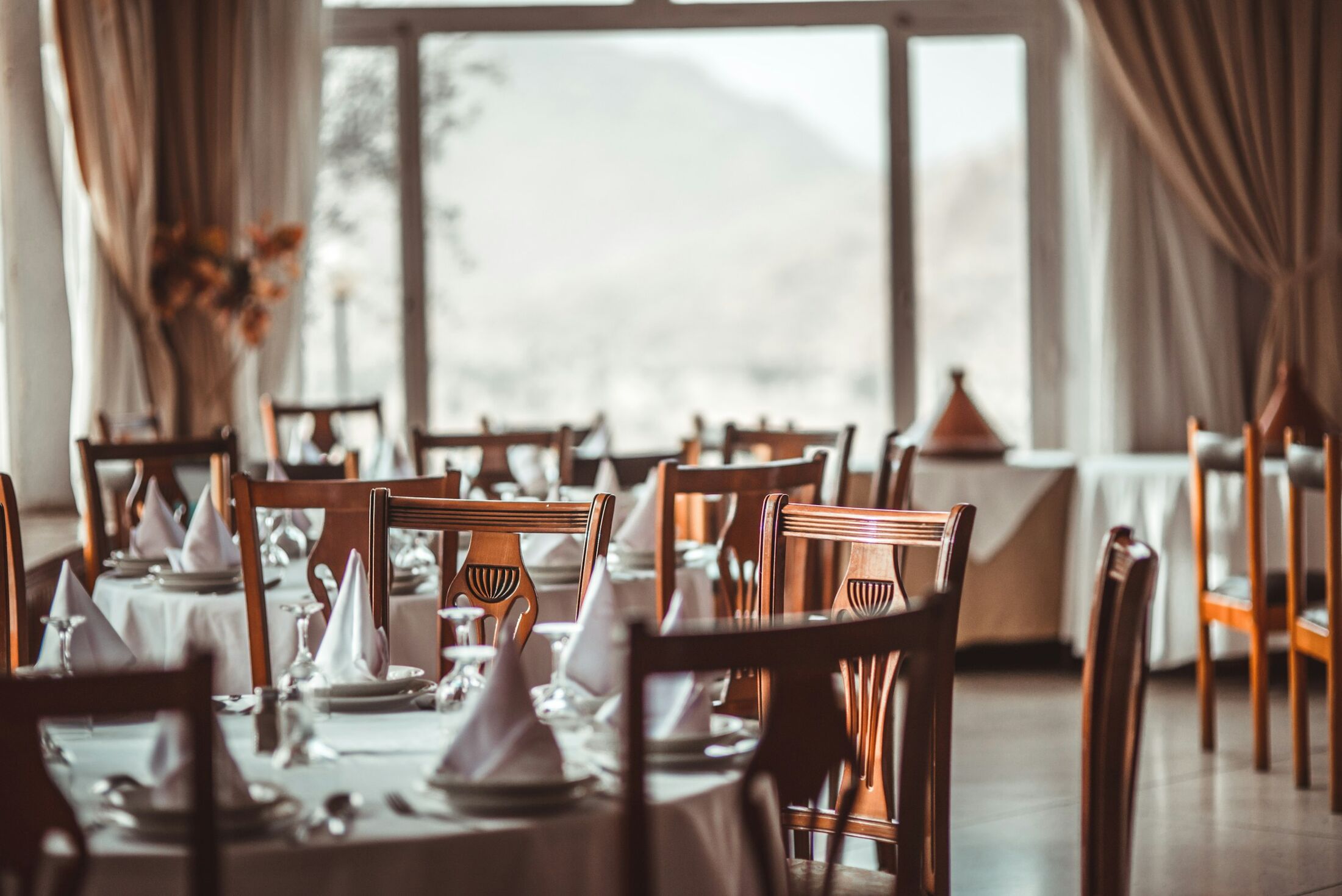 The dining room at lunchtime, tables laid with white linen beside tall windows