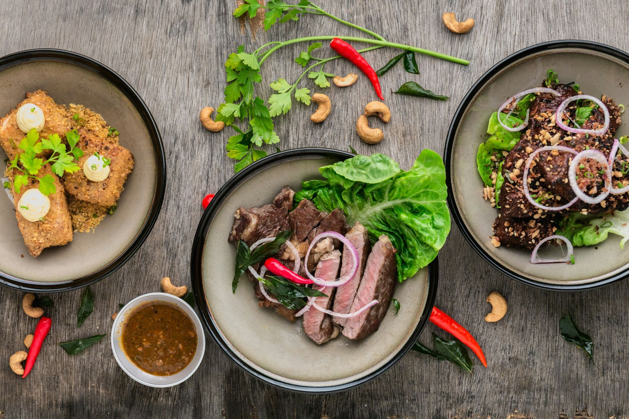 A table spread with sharing dishes: sliced steak, salads and sauces