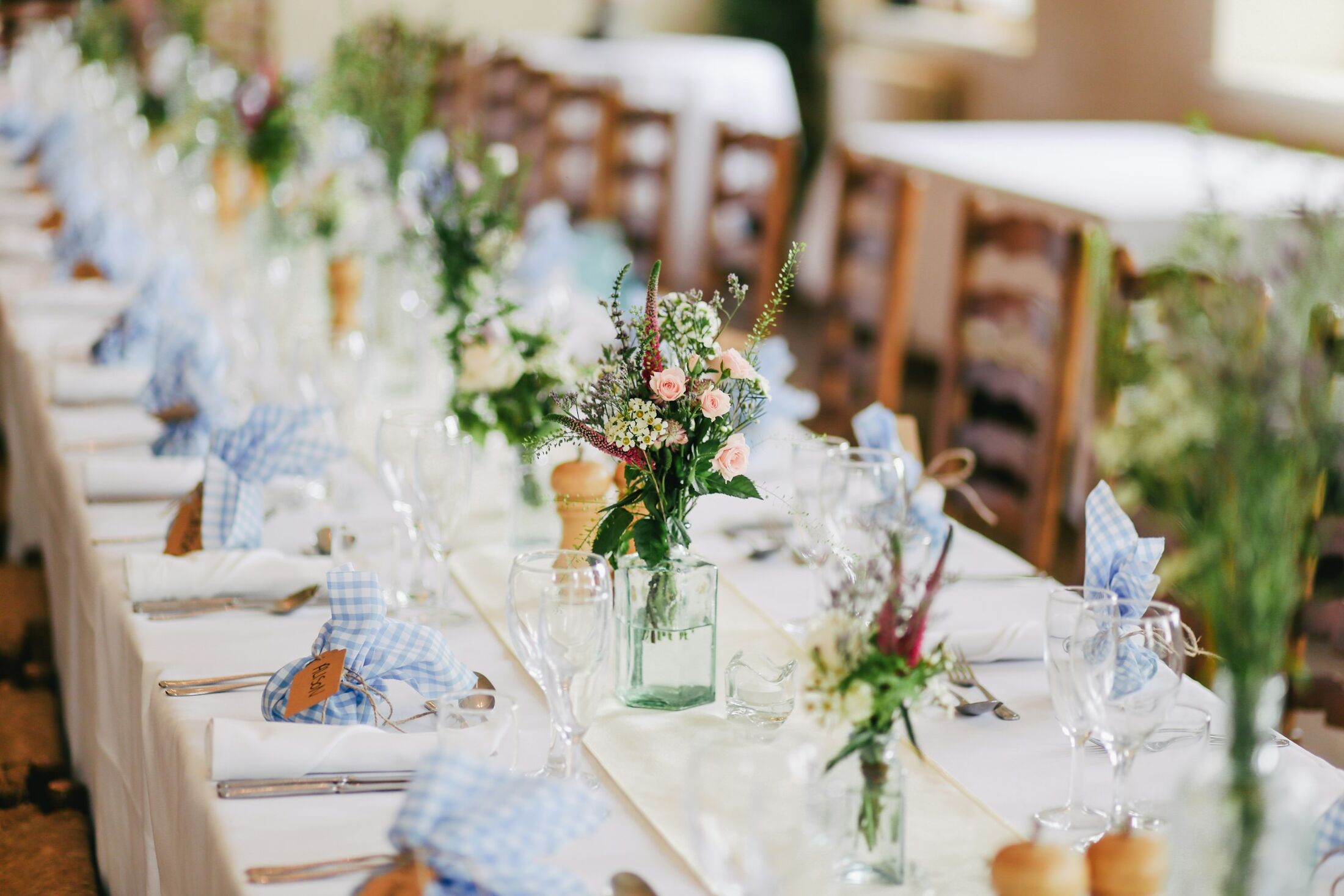 A long wedding table dressed with white linen, glassware and garden flowers