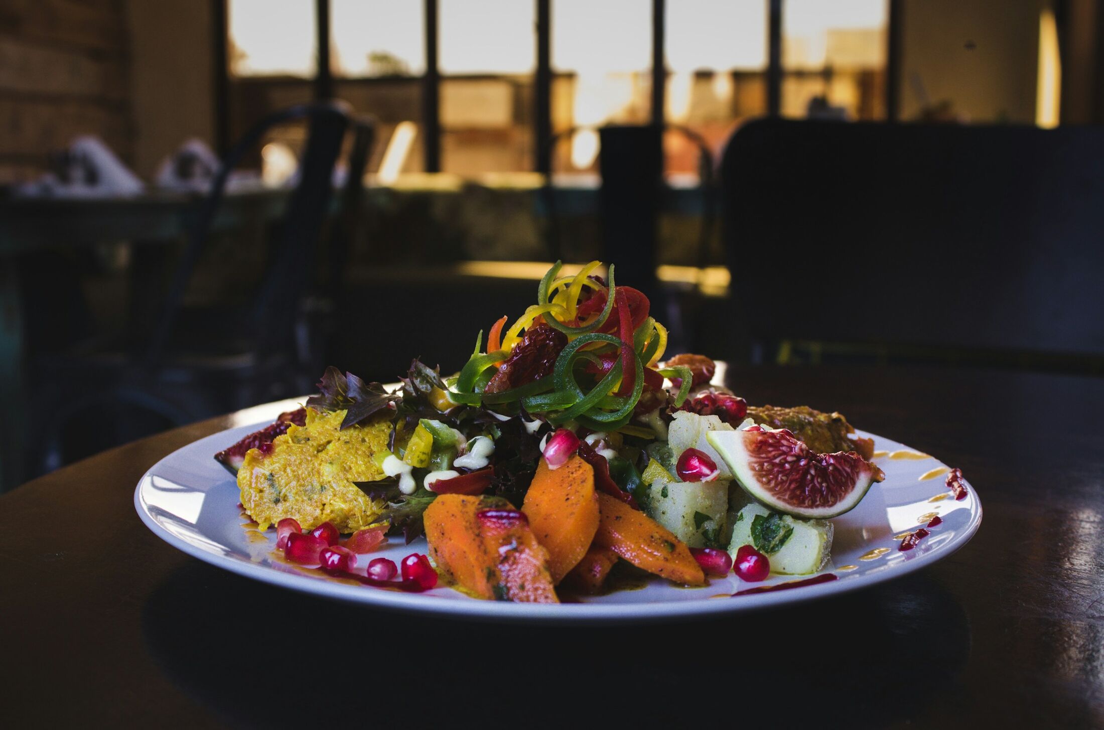 A plated dish of roasted vegetables and fruit under warm restaurant light