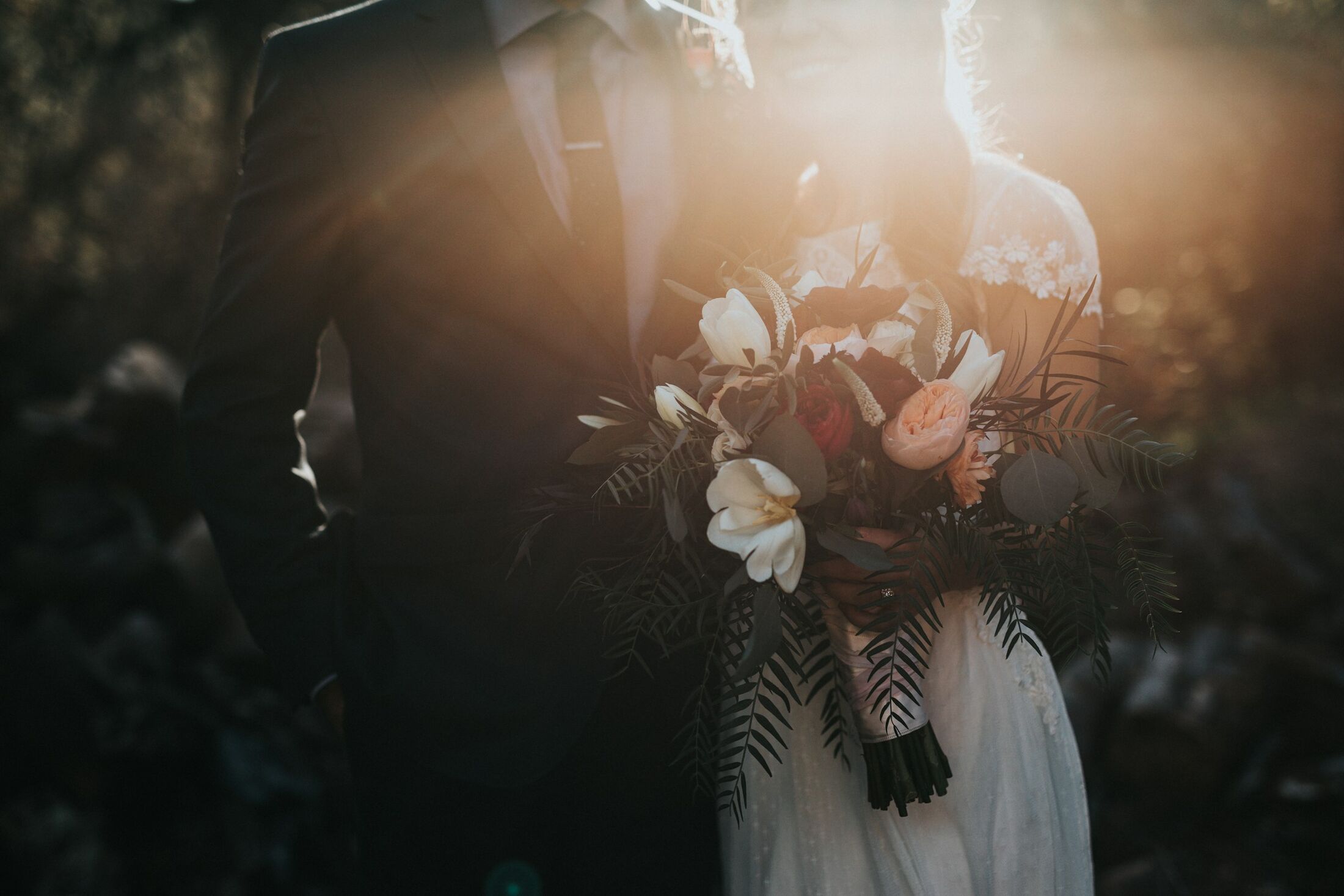 A bride holding a bouquet of dark flowers in soft evening light