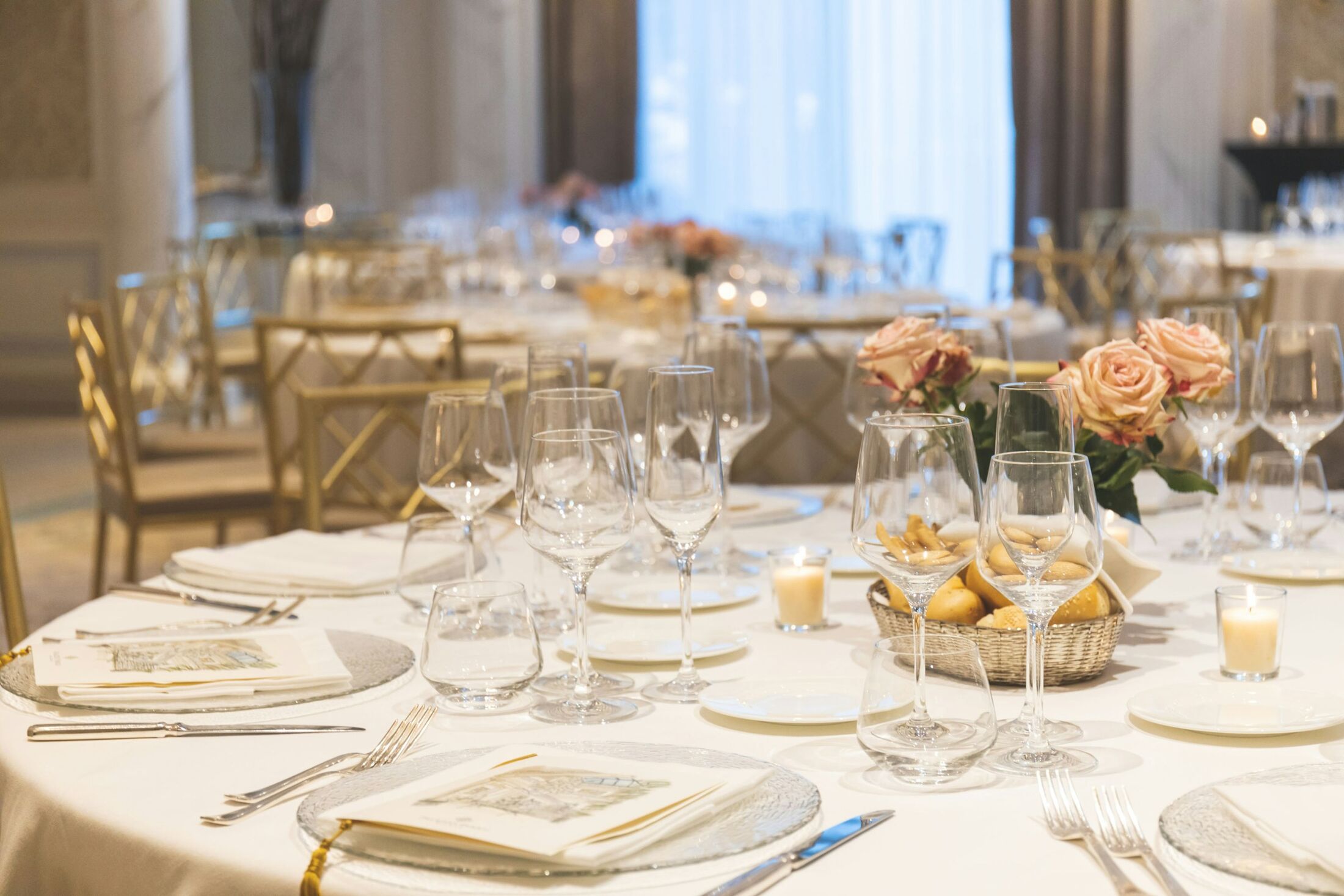 Round tables set for a wedding reception with glassware, candles and pale roses